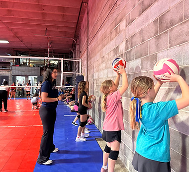 A Storm Performance Volleyball coach instructing young girls on basic setting mechanics during a Storm Volleyball Academy youth training session in Corpus Christi.