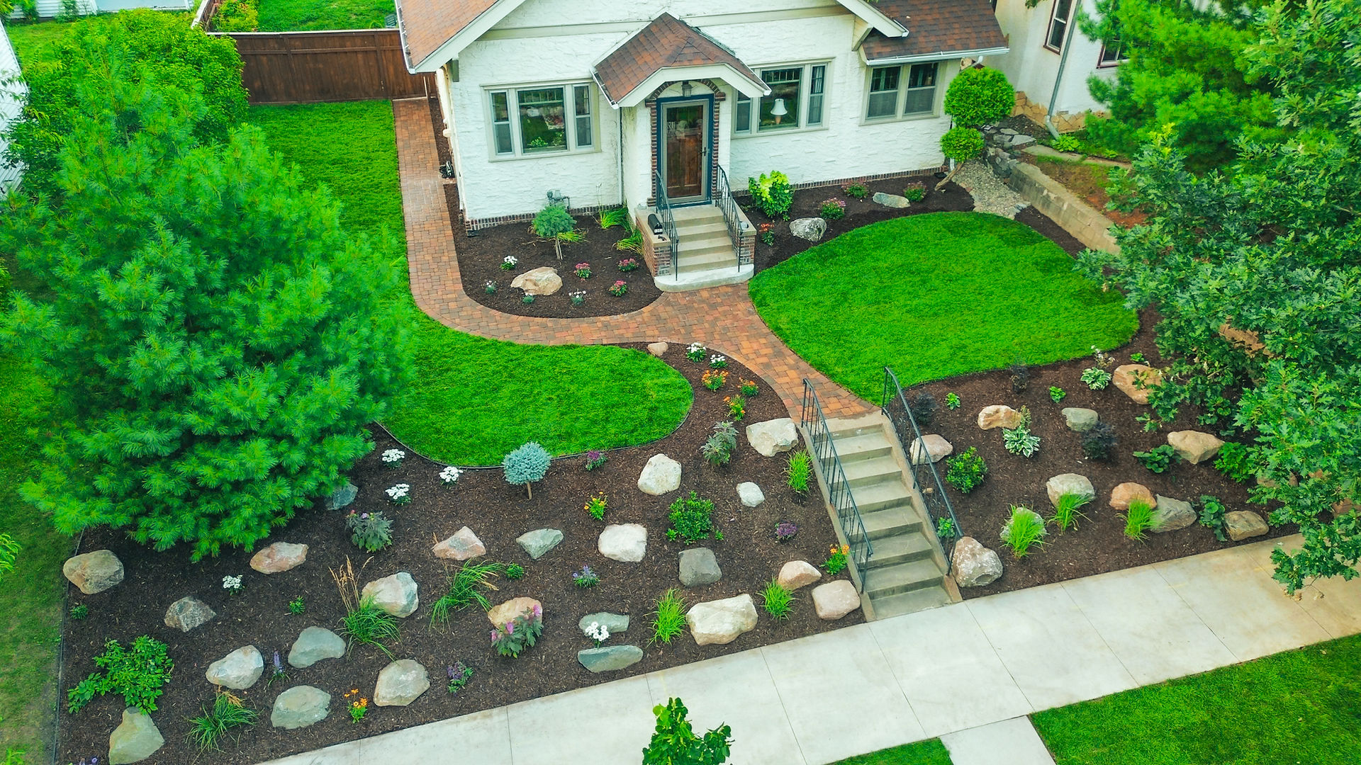Front yard with sweeping brick walkway from sidewalk to porch, boulders, new shrubs and perennials, and fresh mulch.
