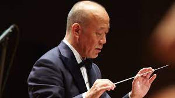 A man in black leather Jacket sitting with one hand on table and other on the face, with blue and white background wall Joe Hisaishi MyMusicSheet