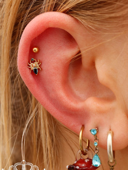 Ohr mit zwei Piercings in Gold mit einem Spinnen Motiv und schwarzem Glitzerstein.