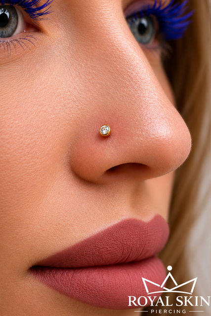 Weibliches Gesicht im Seitenprofil mit roten geschminkten Lippen und ein Nasenpiercing in Gold mit einem kleinen Kristall.
