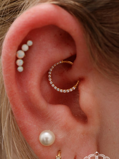 Weibliches Ohr mit diversen Ohrpiercings am Knorpelbereich. Schmuck in Gold mit Kristallsteinen.