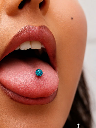 Junge Frau mit rausgestreckter Zunge die ihr Piercing zeigt.