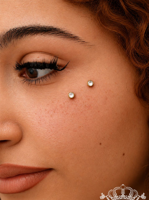 Gesichtspiercing unter dem Wangenknochen in Gold mit Kristallen.