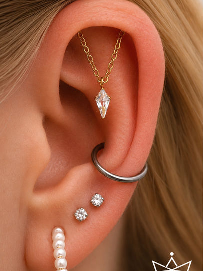 Ein Ohr mit einem Ohrpiercing am oberen Aussenknorpel welches als Kette in Gold runter hängt.