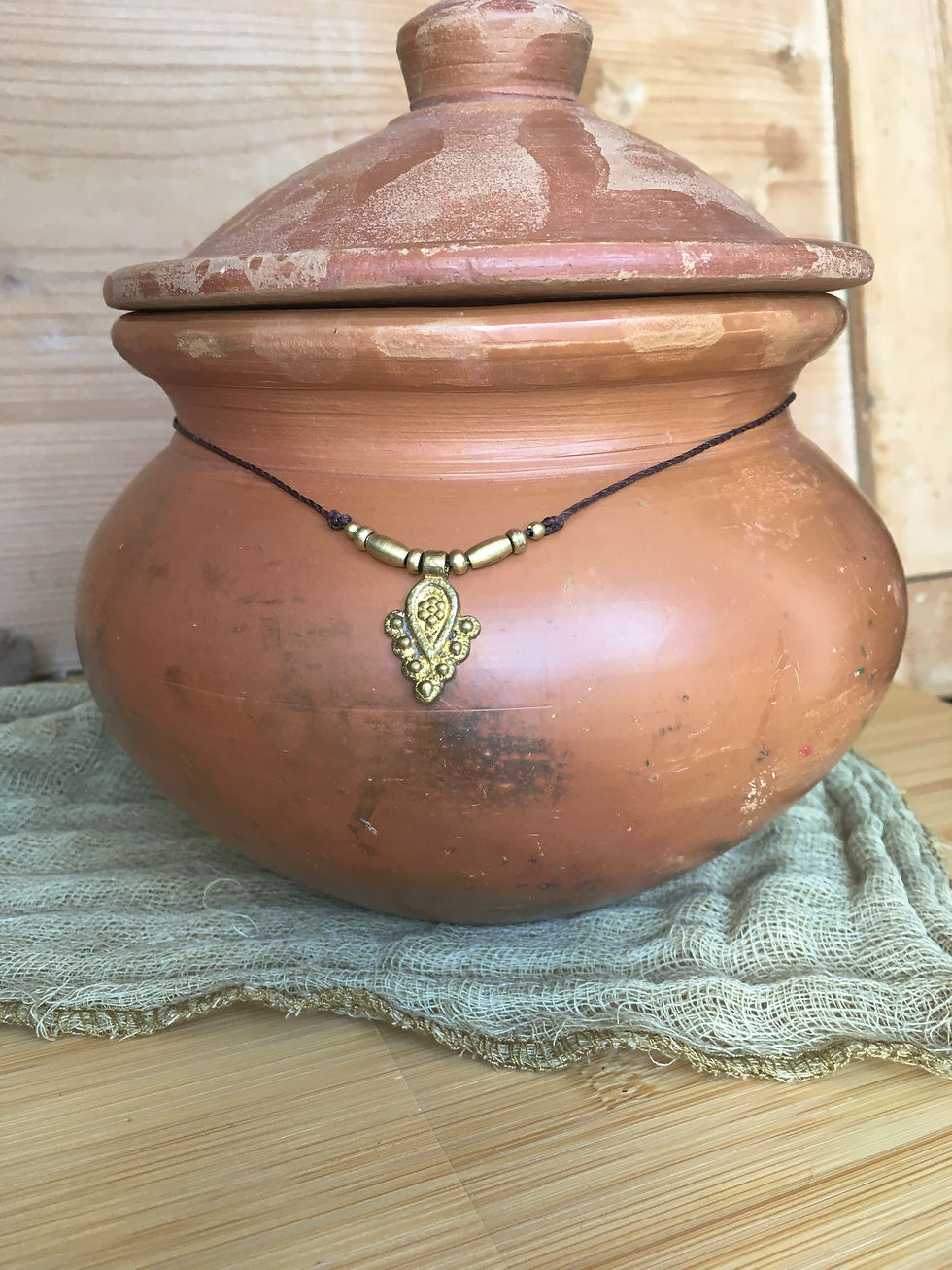 Thumbnail: Dark brown macrame necklace with brass charm displayed on terracotta pot