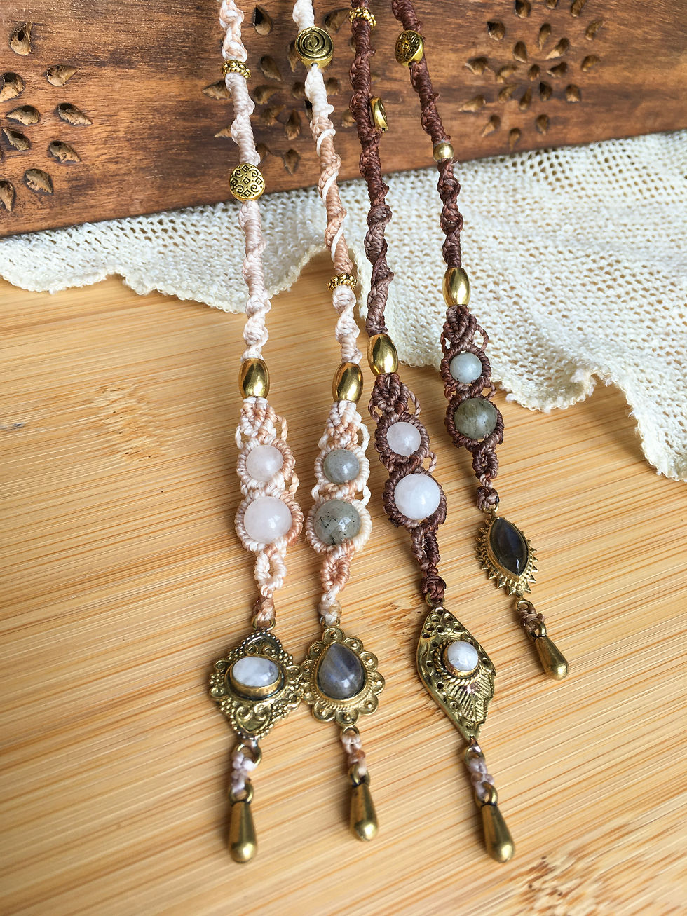 Four macrame hair wraps resting on a wooden surface, showing the gemstone dangle ends and a small section of the woven wraps