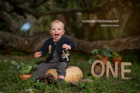 One year old boy smiling during a first birthday portrait session in the morning light