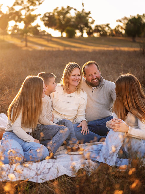 Family sitting together in a sunlit field during a golden hour family photography session in Tarpon Springs, Florida