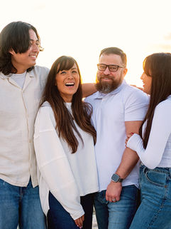 Family of four smiling together during a sunset beach photography session on Honeymoon Island