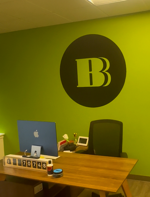 Vinyl logo wall decal with bold black B inside circle on a bright green office wall