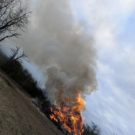 Ein großes Feuer auf einem Feld mit dickem, grauem Rauch, der weit in den Himmel aufsteigt.