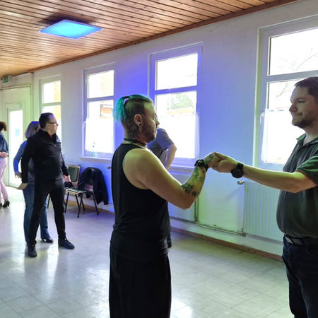 Drei stehende Tanzpaare mit Tanzlehrer im großen Saal des DGHs.