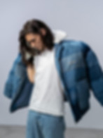 uomo di pelle chiara con capelli lunghi, maglietta bianca e pantaloni jeans, che sta indossando una giacca firmata del brand.