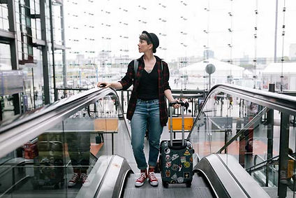 Woman with luggage at the top of an airport escalator, preparing for travel. Ensure your health with our Travel Vaccinations service.