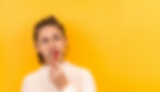 young woman brushing teeth on a yellow background looks up inquisitively