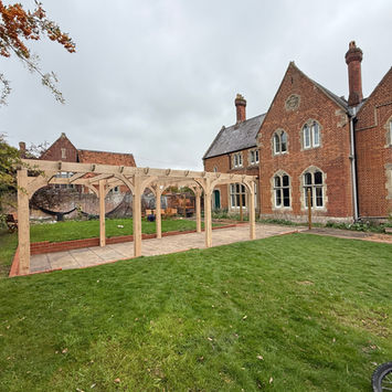 Handmade oak pergola in a landscaped garden, featuring traditional timber joinery and curved braces. Bespoke wooden pergola handcrafted in the UK, Suffolk, ideal for patios and outdoor entertaining spaces.