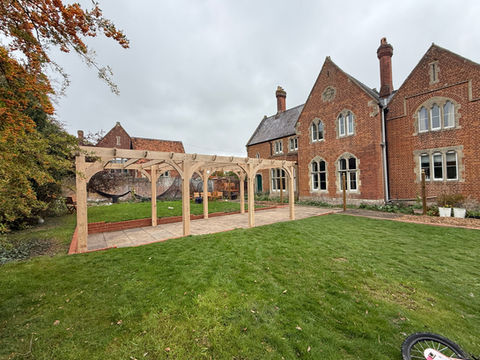 Handmade oak pergola in a landscaped garden, featuring traditional timber joinery and curved braces. Bespoke wooden pergola handcrafted in the UK, Suffolk, ideal for patios and outdoor entertaining spaces.
