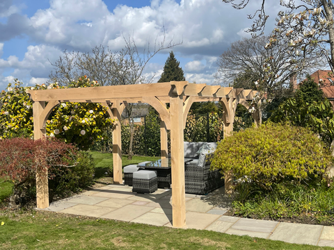 Handmade oak pergola in a landscaped garden, featuring traditional timber joinery and curved braces. Bespoke wooden pergola handcrafted in the UK, Suffolk, ideal for patios and outdoor entertaining spaces.