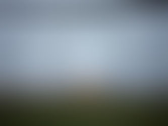A chain-link fence with a torn opening, warm lights blurred in the distance beyond it.