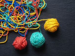 Three balls of brightly coloured yarn — yellow, red, and teal — emerging separated from a tangled mass.