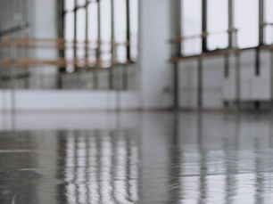 An empty dance studio with a polished floor reflecting the room, light streaming through tall windows.