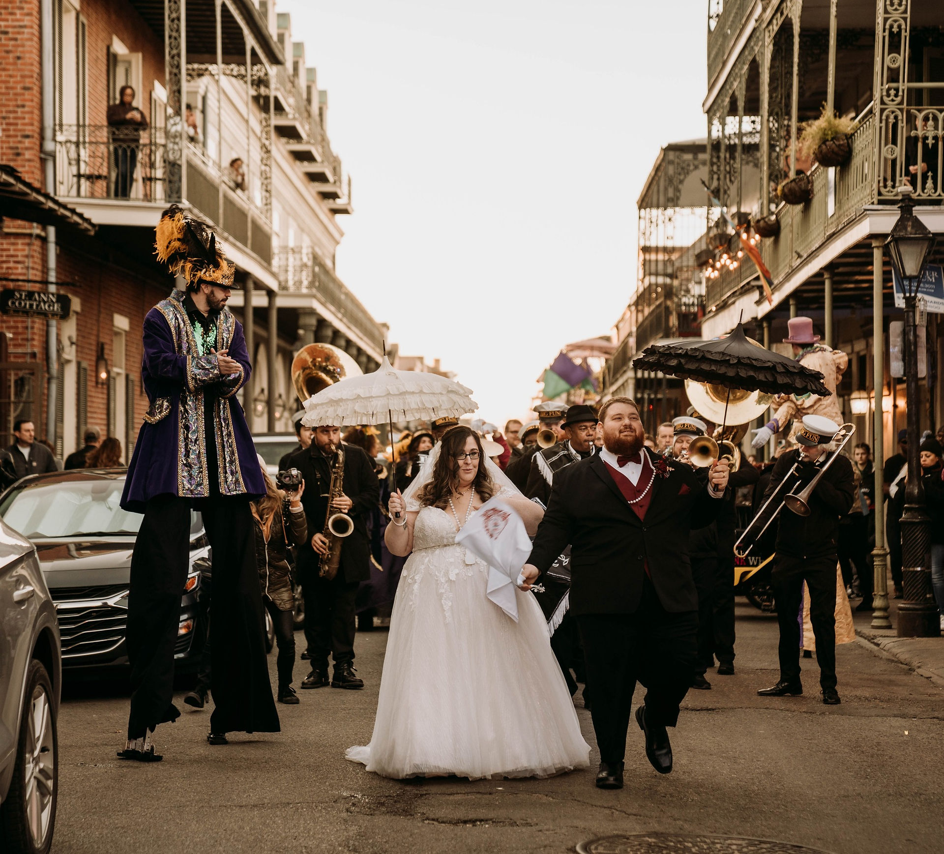 Bride and Groom during their post ceremony wedding second line parade through the New Orleans French Quarter for their january wedding with circus performers, revelers, stilt walkers, and jugglers