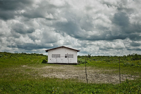 Bare earth field with improvised goalpost and isolated white building, O Jogo, Leandro Martins
