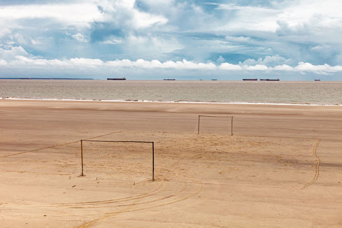 Two goalposts on a wide sandy beach with cargo ships on the horizon, O Jogo, Leandro Martins