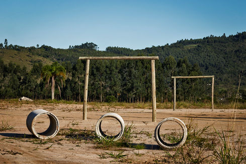 Wooden goalpost beside three concrete rings on a bare earth field, O Jogo, Leandro Martins
