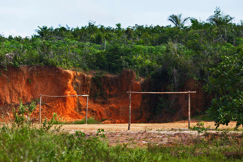 Improvised wooden goalpost before a red clay cliff and forest, O Jogo, Leandro Martins