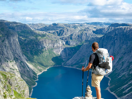 A man on top of a mountain looking down at a lke in the valley