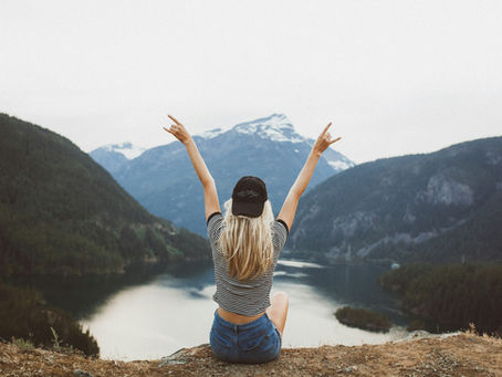 a woman sitting on a cliff facing a lake and mountains