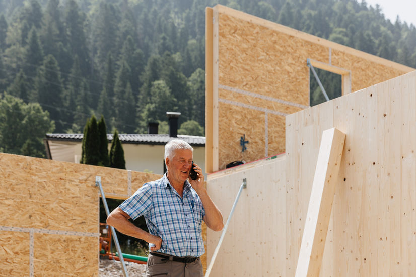 Seniorchef auf der Baustelle mit Mobiltelefon in der Hand im Hintergrund Fortschritt auf der Baustelle
