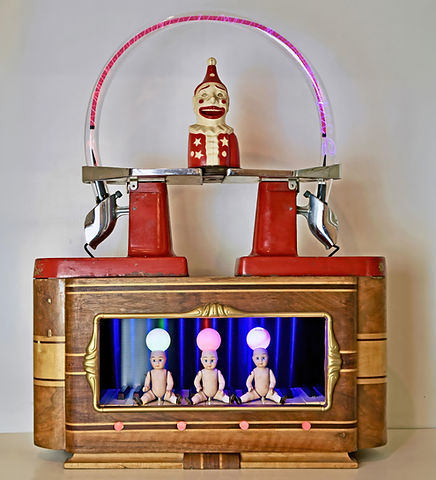 Three glowing baby dolls below a damaged clown and pink arc, built into vintage radio with candy dispensers