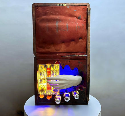 Light sculpture in a repurposed spoon box with circuitry, bulbs, mannequin hand, and velvet panel.
