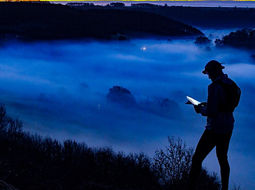 A runner looks at his map at dawn on the edge of the Cotswolds while the valley below is foggy
