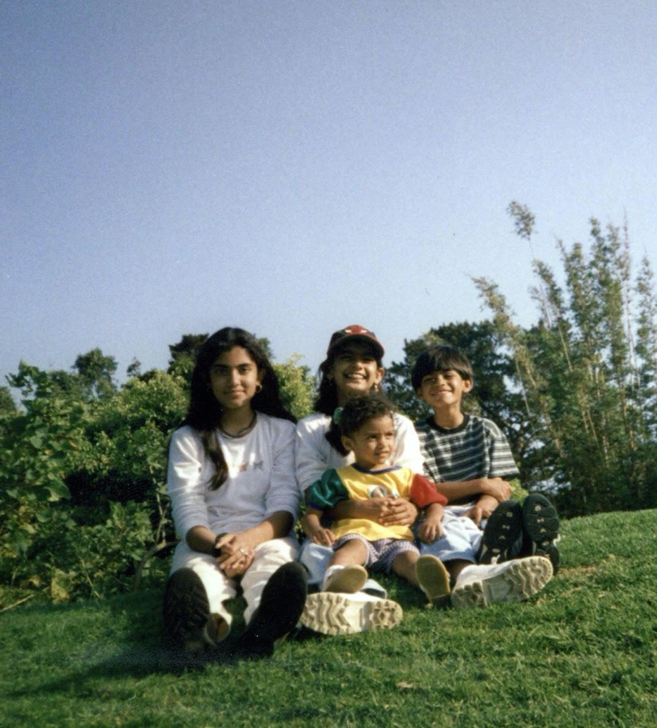 Four siblings smiling and sitting in the grass.