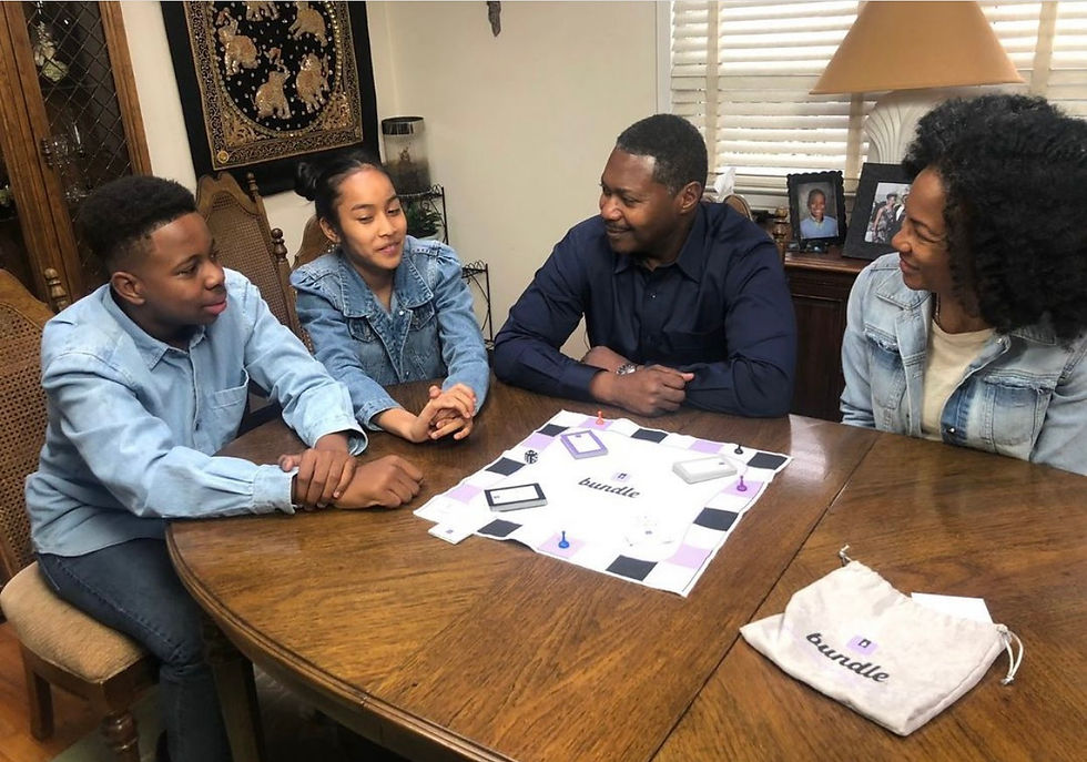 Family of 4 sitting around a kitchen table, They are smiling at each other and laughing. There is a Bundle board game at the center of the table and a Bundle bag on the side of the table.