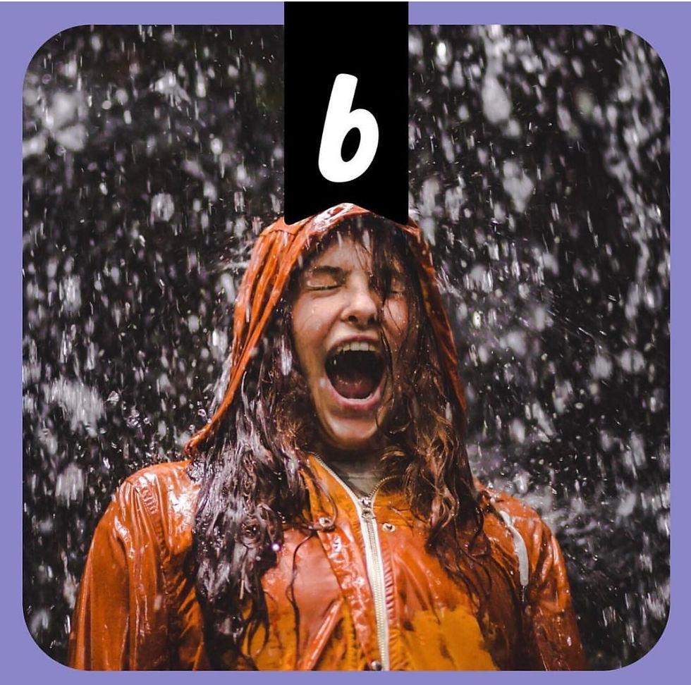 Photo of a young woman wearing an orange raincoat. There is a large amount of rain pouring down on her.