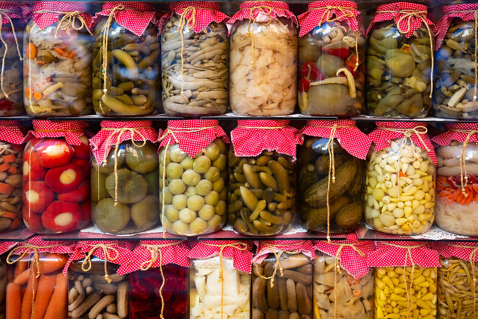 A visually captivating arrangement of assorted pickled vegetables in glass jars, covered with red polka-dot fabric lids and aligned in a vibrant geometric pattern. The jars contain a variety of preserved produce, including garlic, peppers, cucumbers, carrots, and olives. This image radiates color, texture, and tradition, making it ideal for themes related to food culture, natural preservation, culinary arts, or kitchen decor.