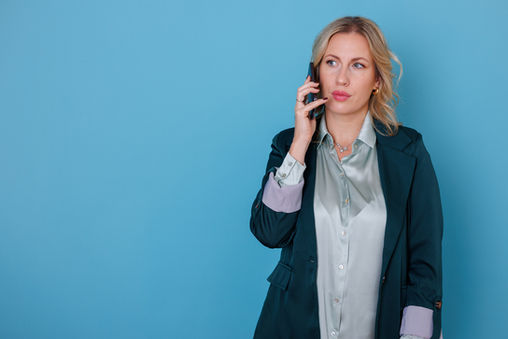 Businesswoman engaged in a phone conversation for networking purposes, discussing work matters against a backdrop of a blue background