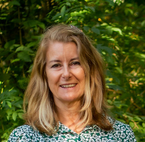 Headshot image of the founder Cate Grundy who is smiling at the camera with a green bush in the background.