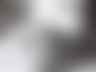 A black and white film photo of some empty bottles and a pot noodle laying in some debris and weeds.