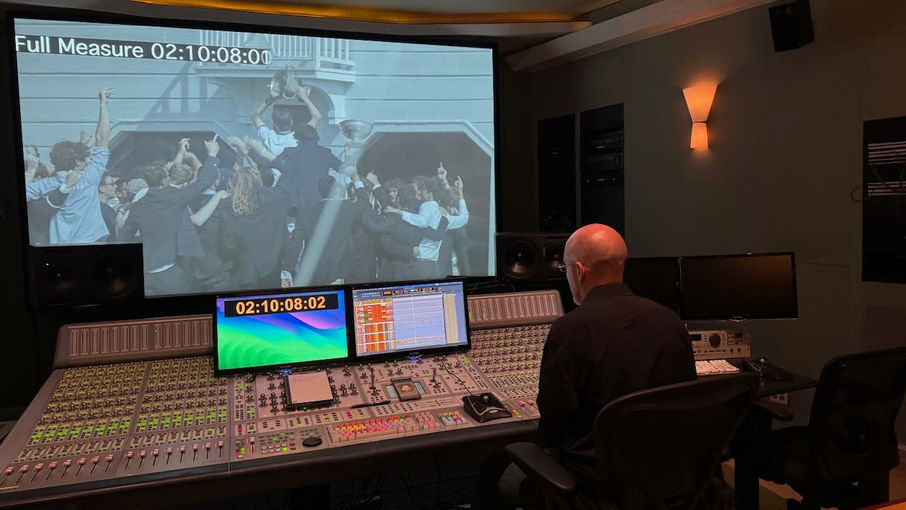 Man at sound board facing large video screen