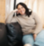 Woman smiling on a black sofa near dresses; Muse Bridal ABOUT US.