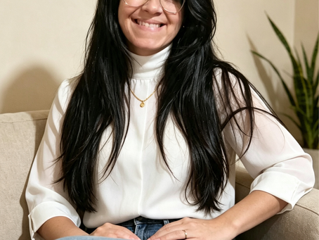 mulher sentada sorrindo cabelos longos lisos pretos blusa branca gola alta cenario atrás bege minimalista sala de estar