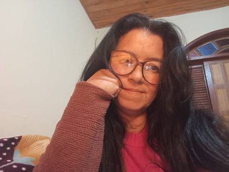Escritora em momento de reflexão sentada no seu home office com cabelos longos e a mão no queixo.
