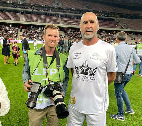 Sébastien Botella en tenue de reporter presse aux côtés d'Eric Cantona sur un stade de football