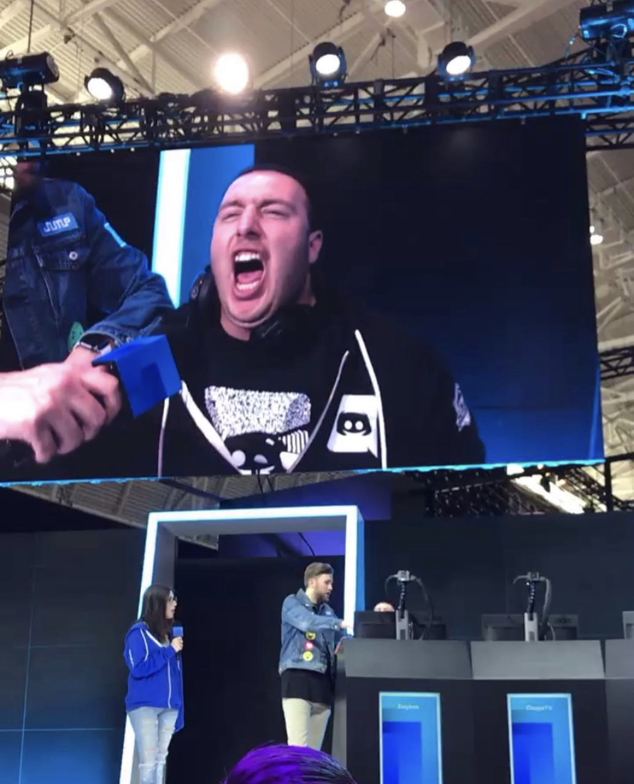 Zaiyken gritando en una pantalla grande, sobre un escenario de evento
